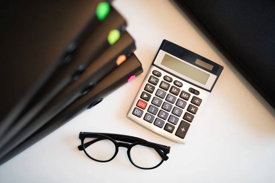 A calculator, glasses and folders on an office desk.