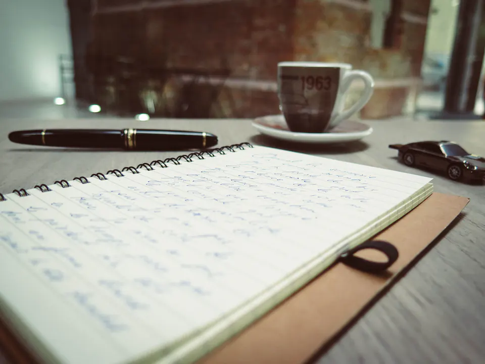 A notebook, pen and coffee on a table.