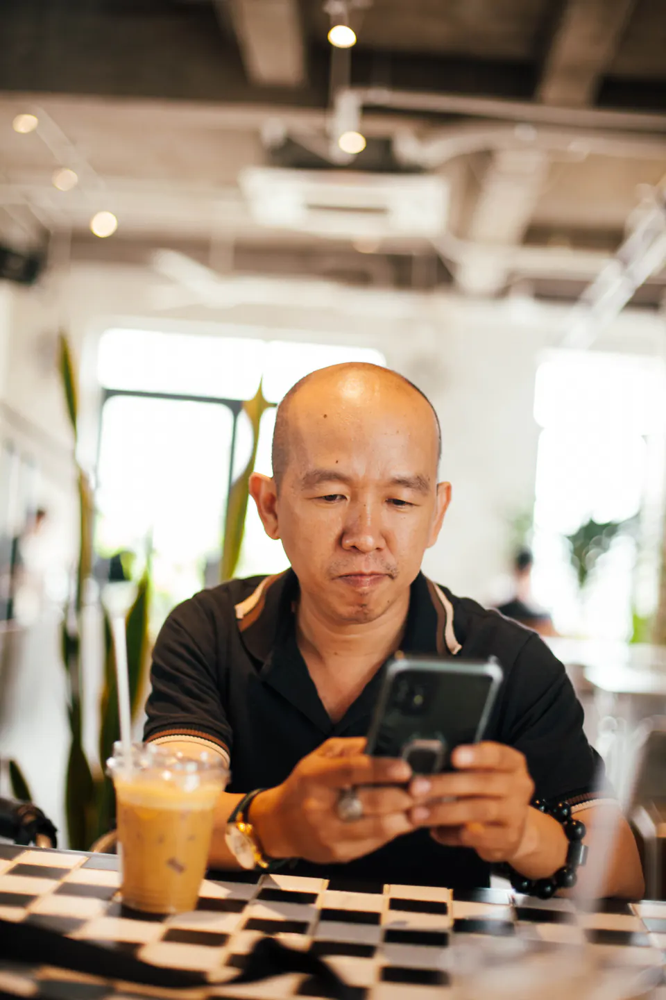 A man checks his smartphone over an iced coffee in a cafe.