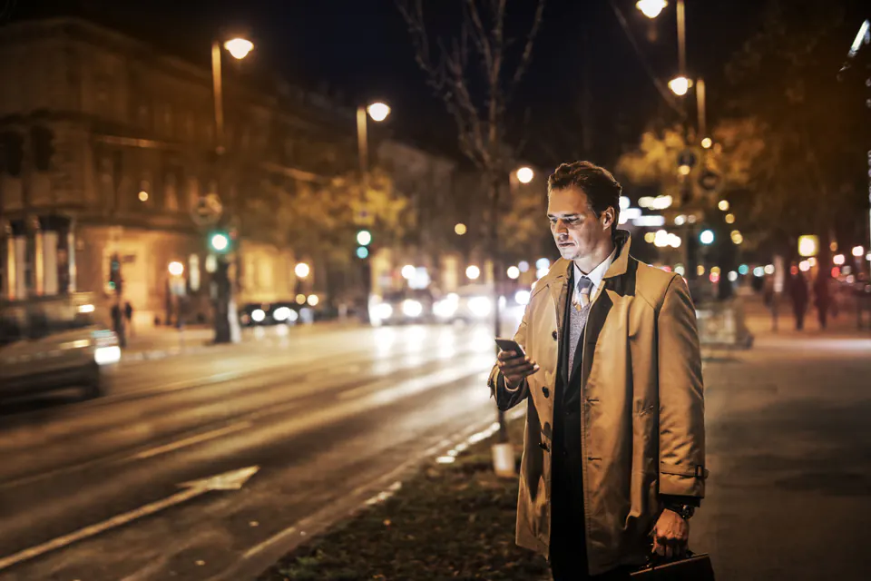 A man in a coat reading his phone on a city street at night.