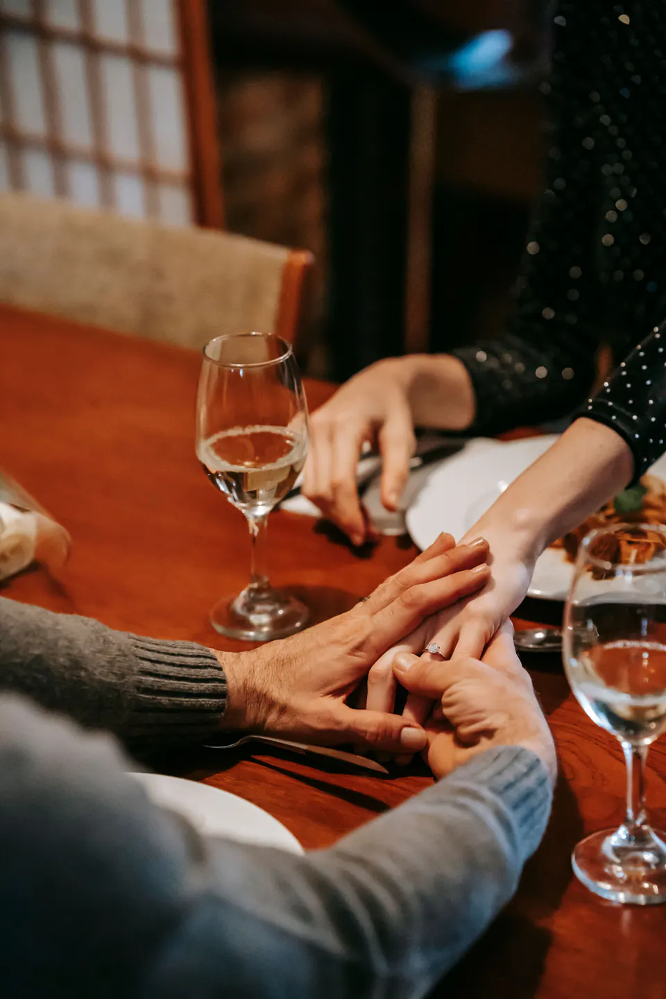 A couple holding hands across a restaurant table at dinner.