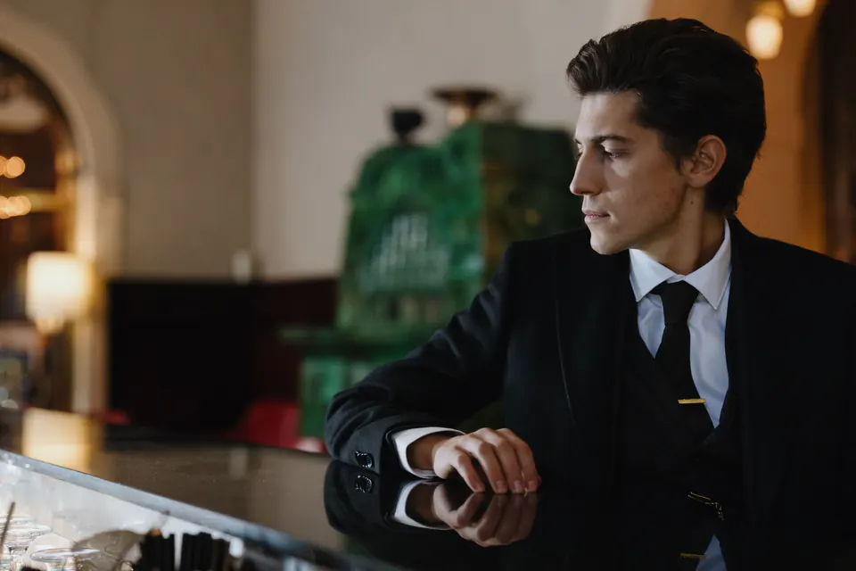 A man in a dark suit waiting alone at a hotel bar.